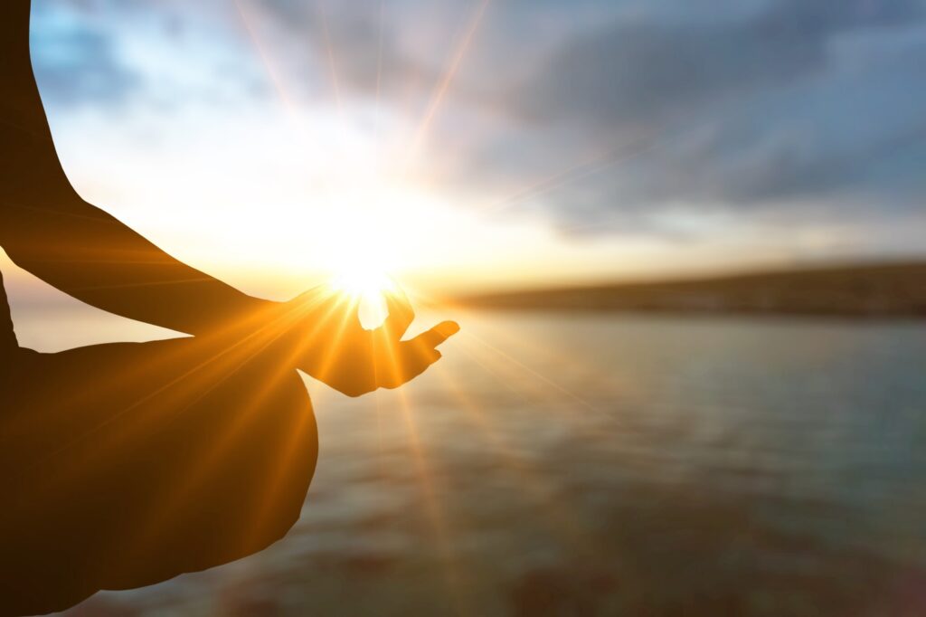 Hände in Meditationshaltung im Gegenlicht über dem Wasser – kostenlose Meditation „Touch Your Soul“